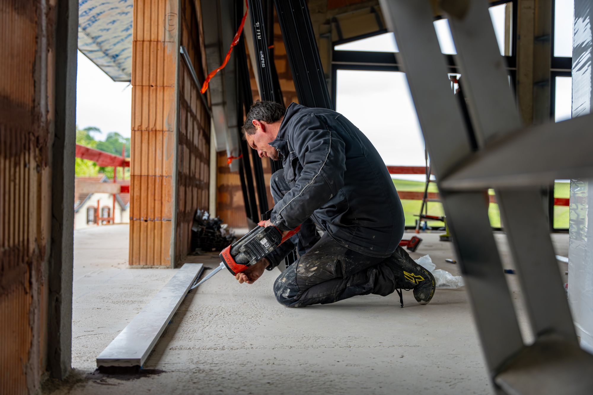Poseur à genoux fixant un profilé sur un chantier, Frechin