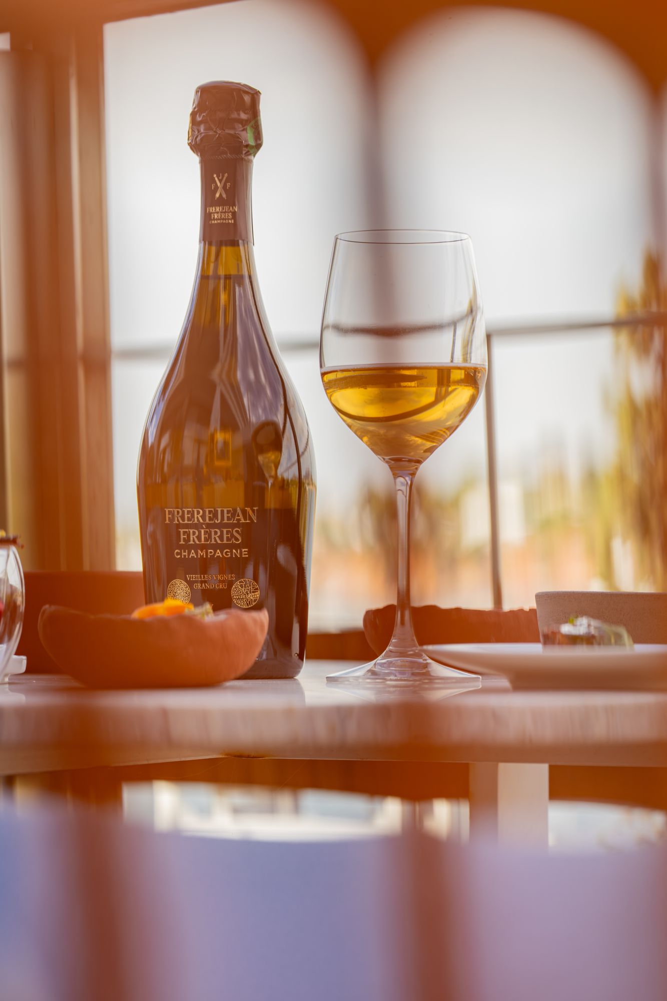 Bouteille et verre de champagne Frerejean Frères devant une fenêtre ouverte sur les vignes
