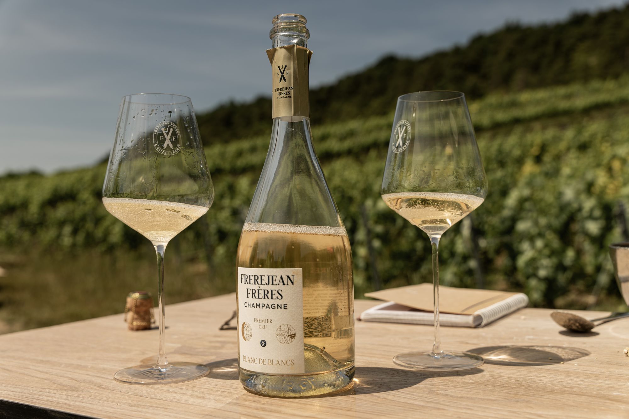 Verres et bouteille de champagne Frerejean Frères sur une table face au vignoble