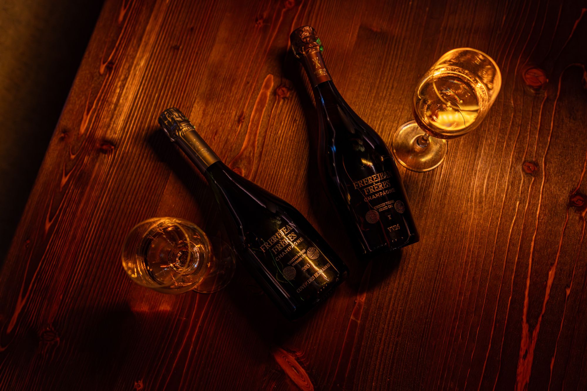 Deux bouteilles de champagne Frerejean Frères posées sur une table en bois, ambiance chaleureuse à la bougie