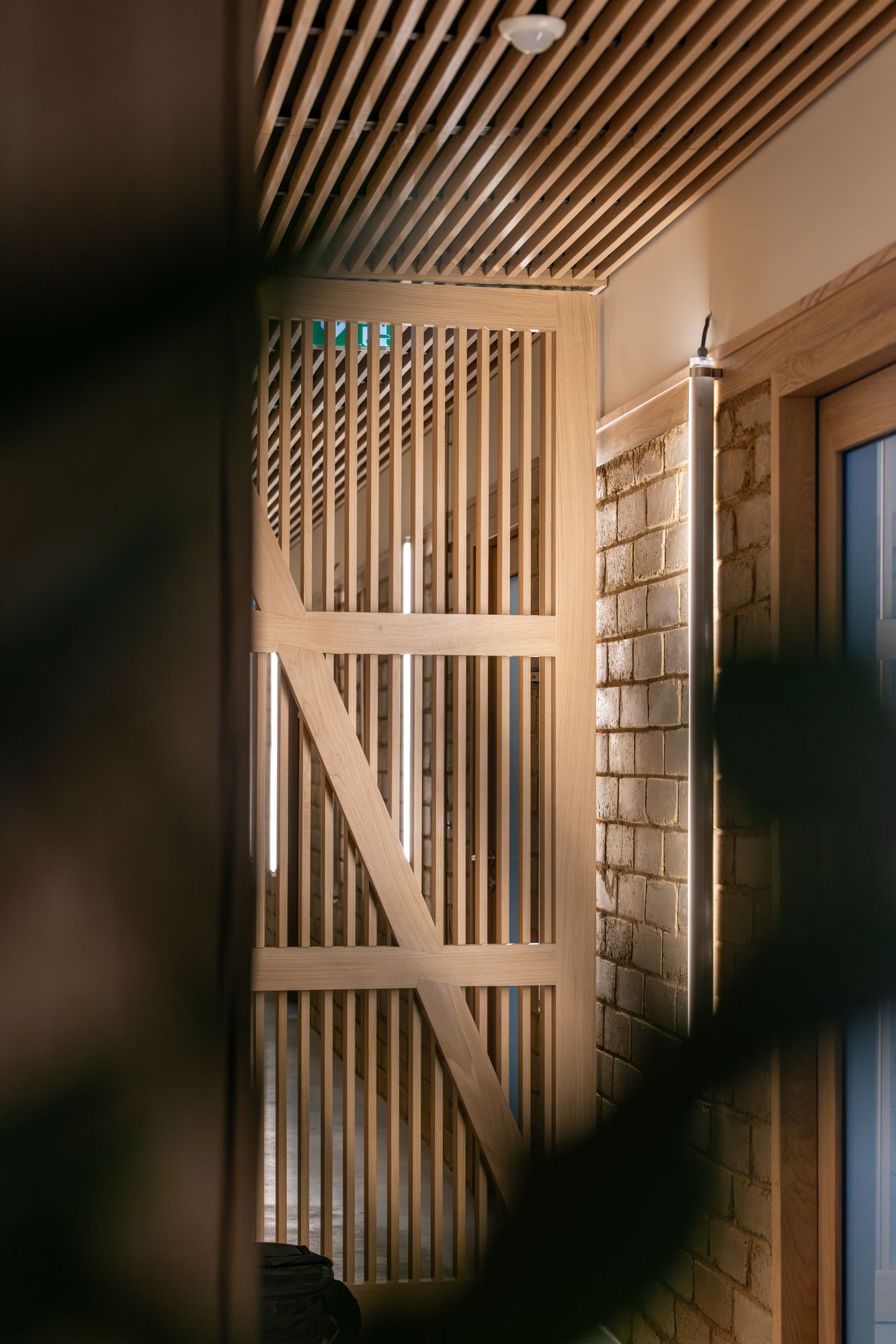 Claustra en bois clair devant une entrée en pierre, Menuiserie Janin