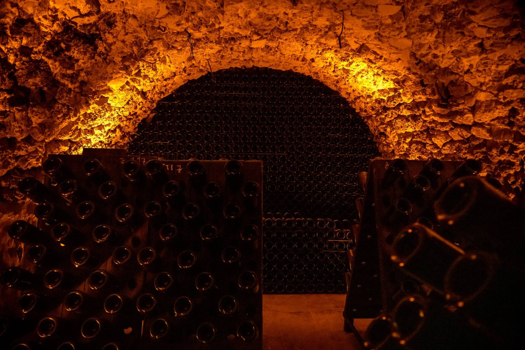 Voûte de la cave de Champagne Tarlant éclairée, bouteilles empilées sur lattes